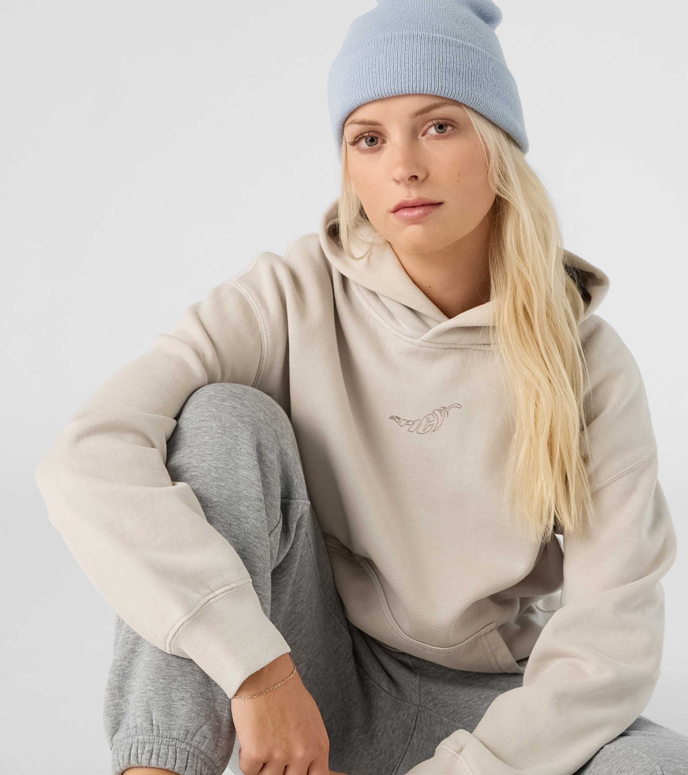 Person wearing bone coloured hoodie with a embroidered spicy logo on a white background. Normalize Neurodivergence.