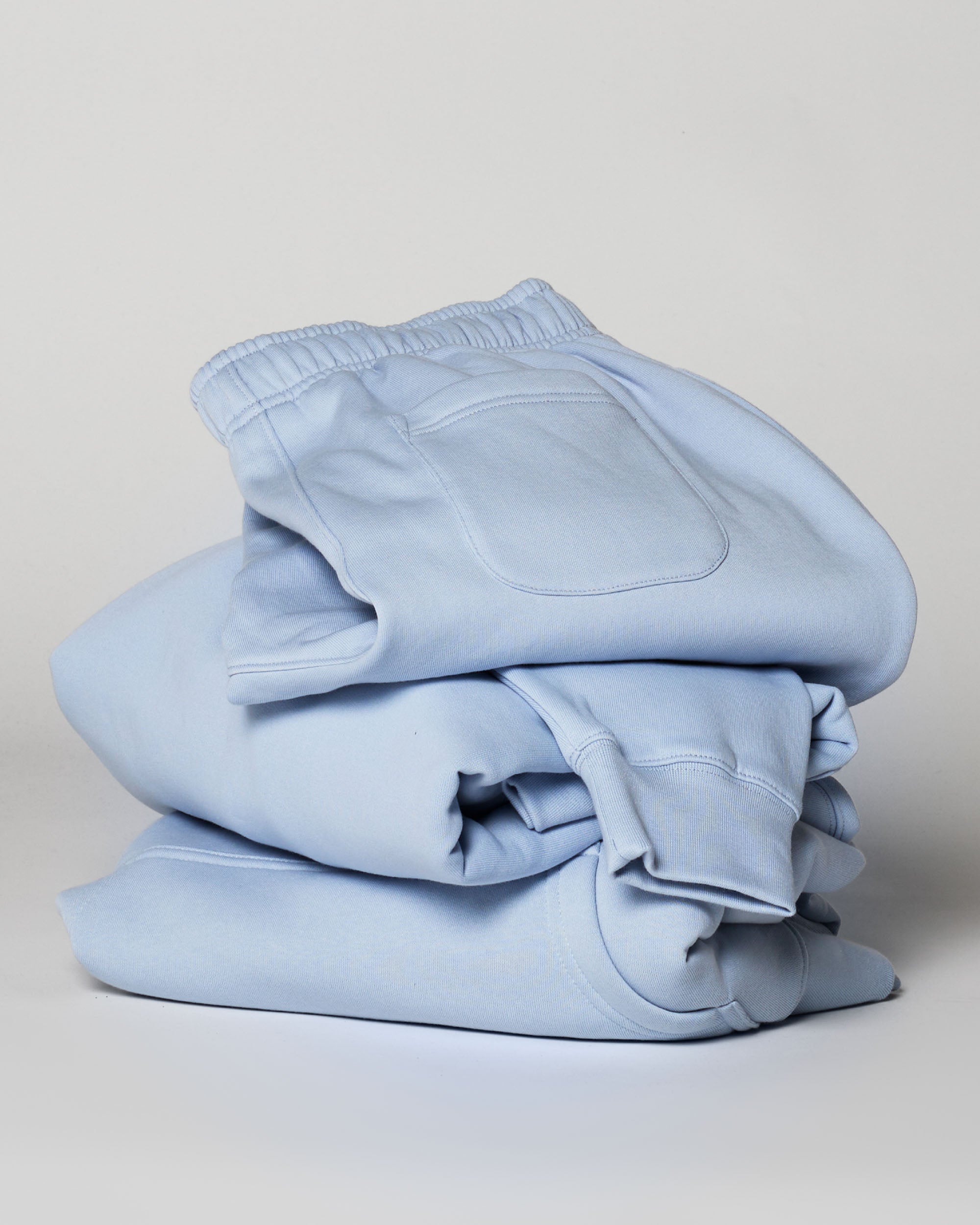 Stack of powder blue track pants on a white background. Flatlay. Normalize Neurodivergence.