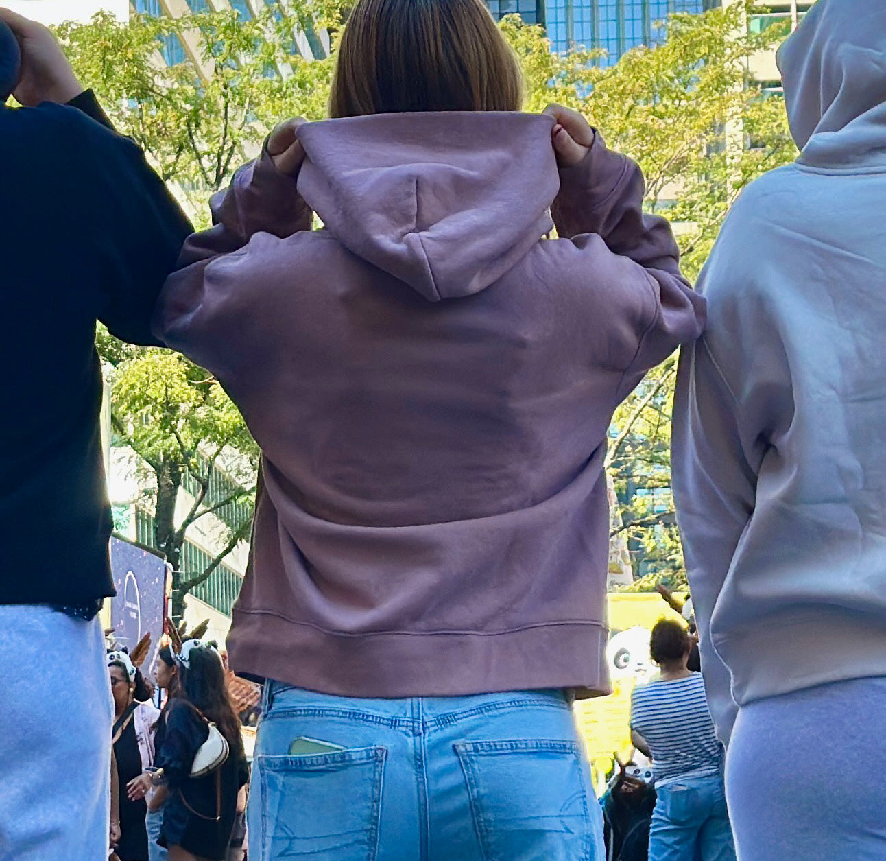 Bone, hazy pink and black hoodies worn by 3 women in front of a city scape. Back view. Normalize Neurodivergence.